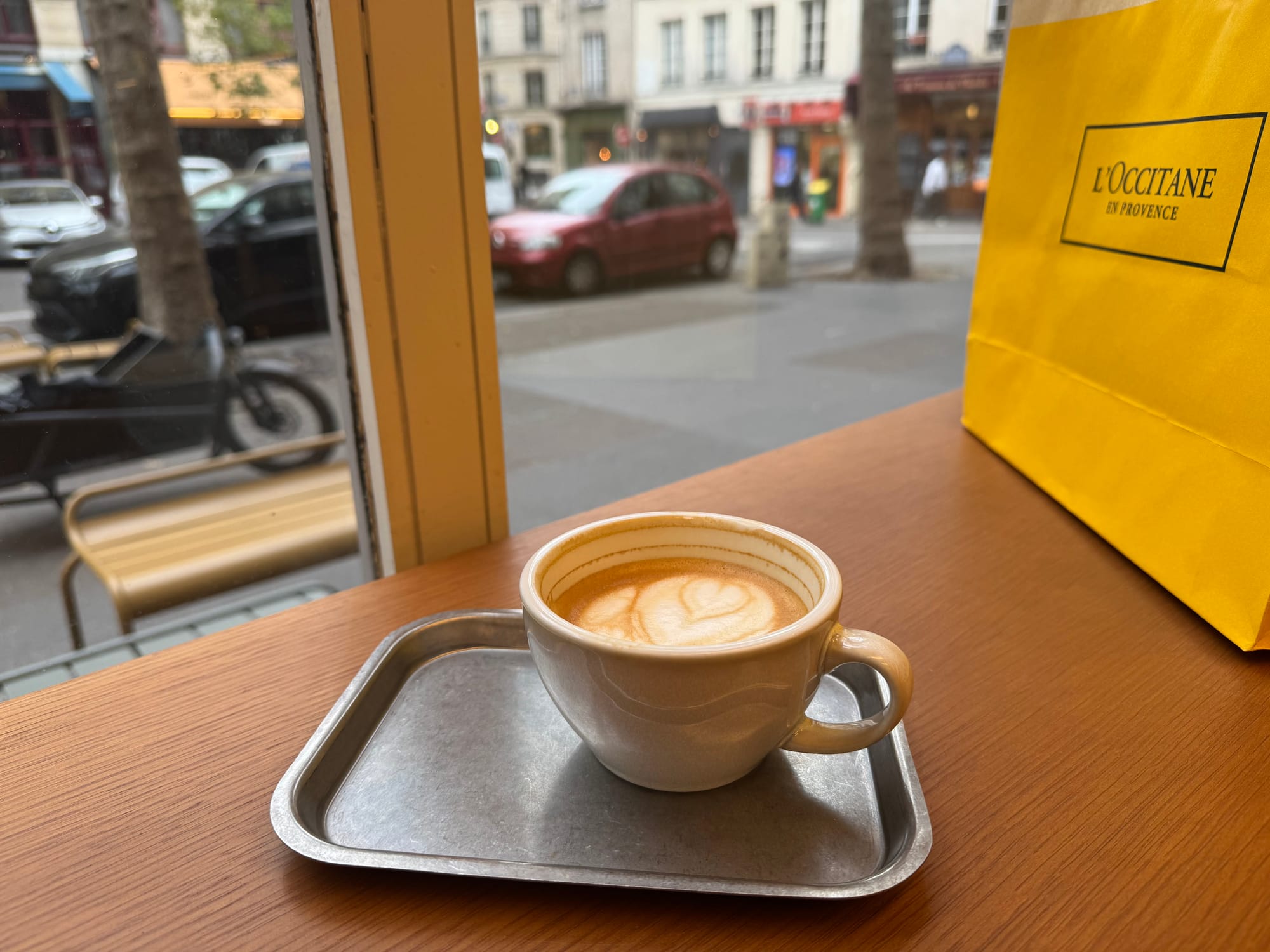 Coffee with coffee flower art by window sill in Paris with L'Occitane shopping bag on the side